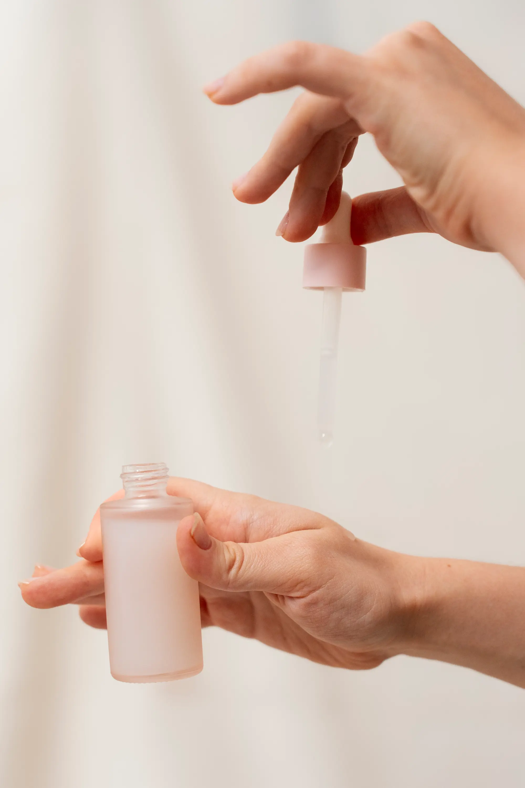 Dłonie z buteleczką serum i pipetą na jasnym, kremowym tle